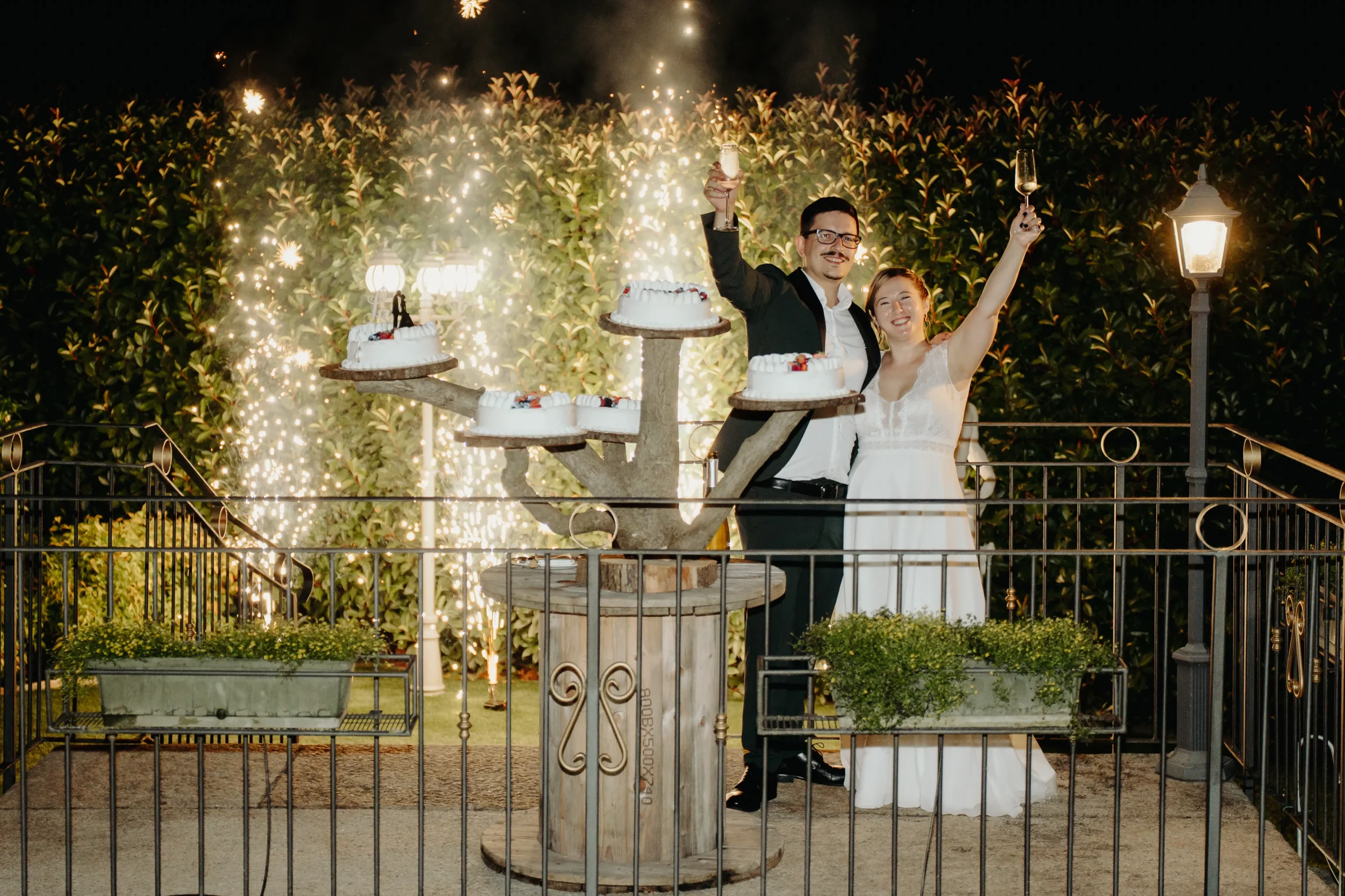 Sposi brindano accanto alle torte con fontane luminose nel giardino della location