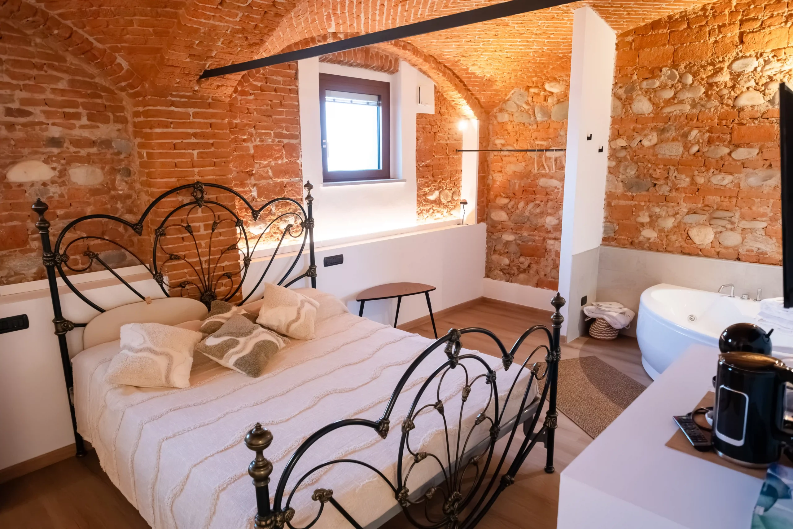 Camera con volte in mattoni, letto in ferro battuto e vasca idromassaggio