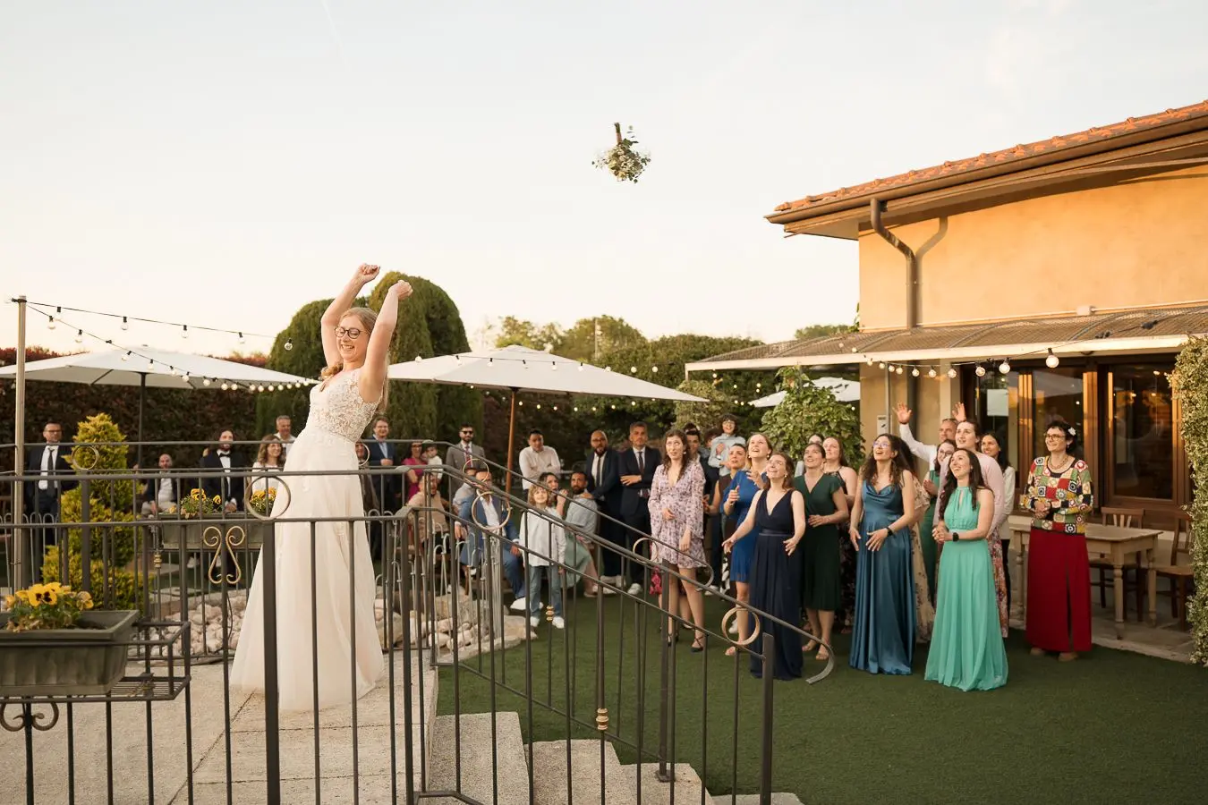 Sposa lancia il bouquet alle invitate nel giardino durante il tramonto