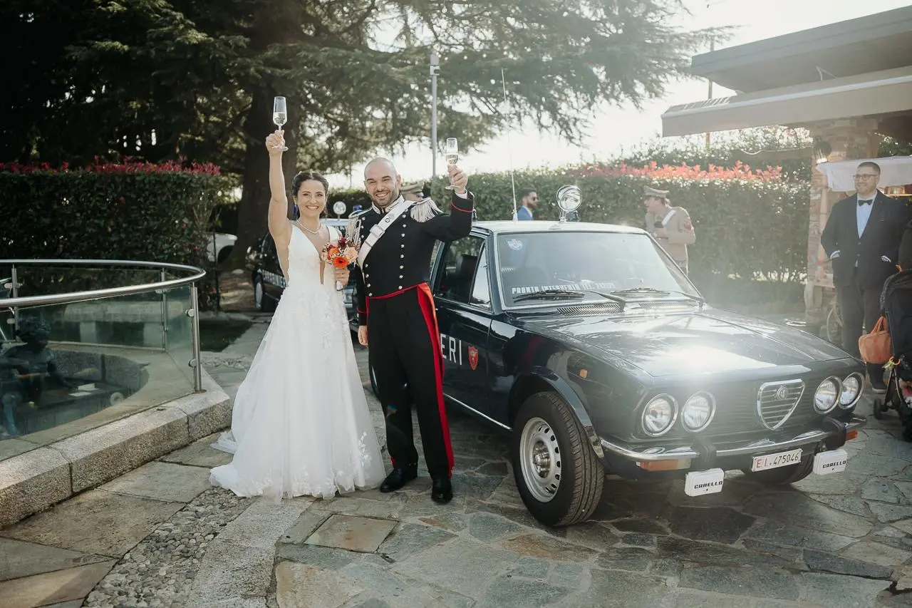 Sposi brindano accanto a un’automobile storica nel cortile della location